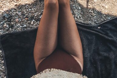 Body Contouring with VASER Liposuction and Renuvion A woman after body contouring procedures sits on a beach under an umbrella