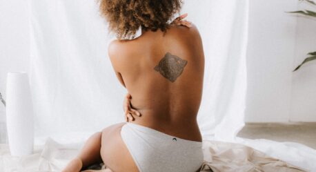 Photo from behind of woman sitting on the floor without a top thinking about a body lift
