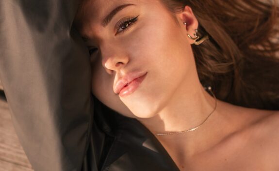 A woman with a lip lift lays on her back on a deck with her arm over half of her face to block the sun {{brizy_dc_image_alt imageSrc=